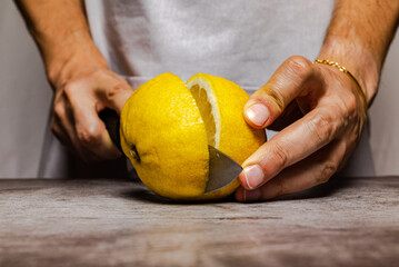 Male hands cutting a ripe yellow lemon with a knife on a slate table. Front view.