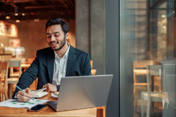 Smiling businessman working with graphs and charts at modern cafe