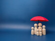 A family of wooden dolls are hiding under a red umbrella, protecting wooden peg dolls, planning, saving families, preventing risks and crises, health care and insurance concepts.
