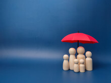 A Family Of Wooden Dolls Are Hiding Under A Red Umbrella, Protecting Wooden Peg Dolls, Planning, Saving Families, Preventing Risks And Crises, Health Care And Insurance Concepts.