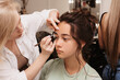 © Anastasia - Shooting in a beauty salon. A makeup artist does eyebrow styling for a young dark-haired girl.