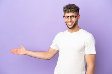 Wall Mural - Delivery caucasian man isolated on purple background extending hands to the side for inviting to come