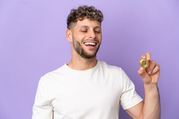 Wall Mural - Young caucasian man holding a Bitcoin isolated on purple background laughing