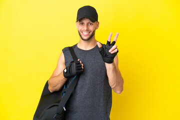 Wall Mural - Young sport blonde man with sport bag isolated on yellow background happy and counting three with fingers