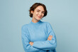 © ViDi Studio - Young confident smiling happy caucasian woman wear knitted sweater look camera hold hands crossed folded isolated on plain pastel light blue cyan background studio portrait. People lifestyle concept.