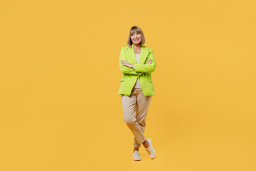 Wall Mural - Full body smiling fun elderly woman 50s year old wearing green jacket white t-shirt hold hands crossed folded look camera isolated on plain yellow background studio portrait. People lifestyle concept