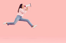 Side View Happy Joyful Excited Woman In Pink Sweatshirt And Blue Jeans Hurrying To Share Urgent Information, Jumping High On Pastel Pink Copy Space Background, Flying In Air, Yelling Through Megaphone