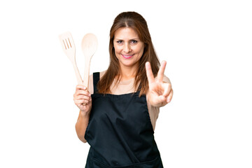 Canvas Print - Middle age caucasian woman holding a rolling pin over isolated background smiling and showing victory sign