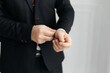 © Evgenii - Close-up of a man in a suit adjusting a button on his shirt.The businessman adjusts the button on his white shirt. A cropped shot of a businessman in a suit adjusting cufflinks.
