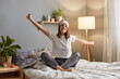 © sementsova321 - Indoor shot of smiling satisfied delighted woman wearing sleeping mask sitting on bed in cozy bedroom and stretching her arms, waking up in good mood, enjoying weekend morning.