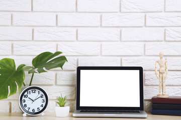 Poster - Laptop computer with green leafs, round clock and wooden figure on brick wall background