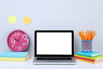 Laptop computer with books, pencils and round clock on grey background