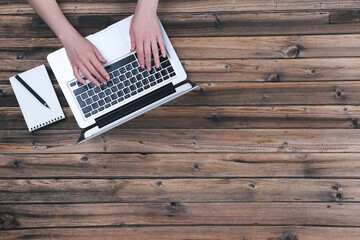 Poster - Woman working on laptop computer with notepad and pen on wooden table