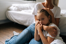 Portrait Of Sad Little Girl Looking At Camera And Loving Caring Mother Comforting Offended Afraid Child Daughter, Showing Love And Care, Expressing Support, Hugging And Stroking Hair Sitting On Floor.