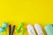 © Goncharuk film - Active living concept. Top view photo of green dumbbells, skipping rope, exercise mat, bottle of water and white sports shoes on yellow background with copy space. Minimal fitness idea.