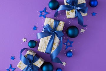 Wall Mural - New Year concept. Flat lay composition made of present boxes with blue bows, Christmas baubles, sequins, stars on violet background.