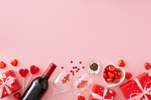 Valentine's Day concept. Top view photo of red gift boxes, wine bottle with glasses, heart shaped saucers with candies and lollipops, sprinkles on pastel pink background. Flat lay with copy space.