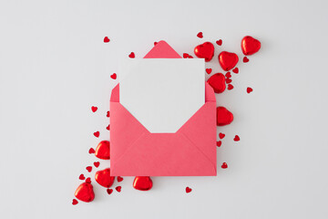 Love or Valentines concept. Flat lay composition made of envelope with letter, heart shaped chocolate candies and sprinkles on white background. Sweet Valentines card idea.