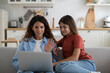 © DimaBerlin - Smiling positive woman nanny and school age girl making video call in laptop contacting parents teenager. Kind caring mother waving hand greeting Internet interlocutor sits on couch with daughter