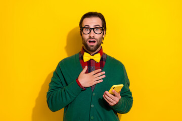 Photo portrait of young nice guy spectacles hold gadget nervous amazed wear trendy green garment isolated on yellow color background