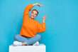 Photo of adorable pretty lady wear orange sweatshirt sitting platform pointing two finger empty space isolated blue color background