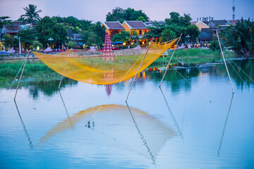 Wall Mural - A fishing net suspended on poles over a river running past an historic village at Hoi An in Vietnam