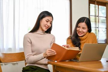 Wall Mural - Two happy Asian female college friends research some information in the book