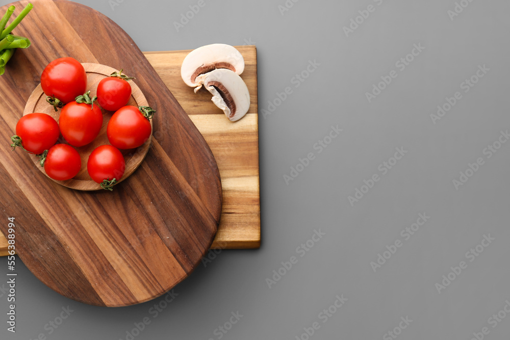 Wooden cutting board and fresh vegetables on grey background