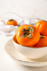 Wall Mural - Bowl of ripe persimmons on light background, closeup