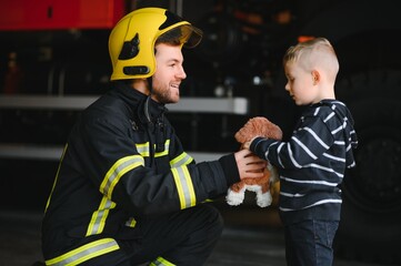 Dirty firefighter in uniform holding little saved boy standing on black background.