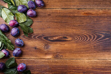 Freshly Harvested Ripe Plums With Green Leaves Border A Text Free Space Right On Weathered Wood Boards As Background