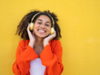 © gonzagon - Young african american teenage girl listening to music happily with headphones over yellow wall
