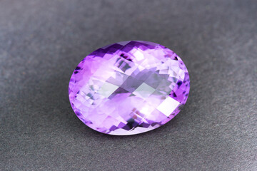 Natural Uruguay amethyst gemstone. Oval checker faceted, big size violet or purple color loose crystal clear stone setting for making jewelry. Gray textured paper background. Gemology, mineralogy.