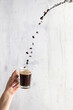 Ziarna kawy sypiące się do filiżanki z zaparzoną kawą, ręka trzymająca filiżankę kawy