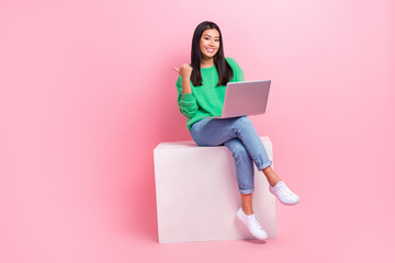 Wall Mural - Full length photo of charming cheerful person sit podium use netbook indicate finger empty space isolated on pink color background