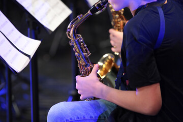 Wall Mural - A person playing the saxophone by notes sitting in a jazz orchestra a close-up view of a musician blowing into a musical instrument