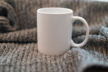 empty white cup mockup for design on knitted sweater background in winter