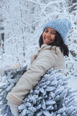 Wall Mural - There is a smiling woman holding a snowy Christmas tree out in the winter forest with a smile on her face