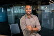 © Liubomir - Portrait of african american businessman in office, man in shirt standing near window smiling and looking at camera, programmer working inside development company.