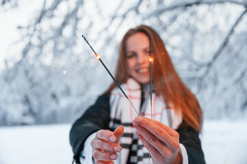 Holding new year sparklers. Beautiful young woman is outdoors in the winter forest