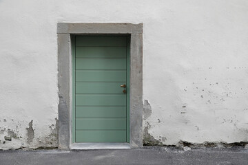 Old green closed house door, stone house wall with cracked surface, no person