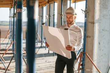 Wall Mural - Manager is in the formal clothes. Holding plan in hands. Man is working on the construction site at daytime