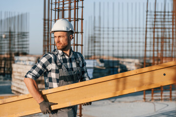 Wall Mural - Man is working on the construction site at daytime. Moving the big wooden plank