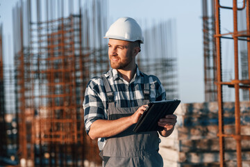 Wall Mural - Looking to the side. Holding tablet. Man is working on the construction site at daytime