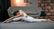 © standret - Stretching exercise. Young woman with slim body type in white sportswear is indoors doing yoga