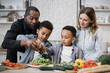 © sofiko14 - Portrait of smiling mom, dad and little sons adding olive oil to the salad while cooking in kitchen together. Happy multiracial parents and small boys kids have fun preparing healthy food at home.