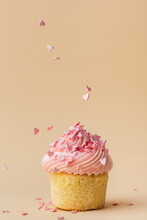 Close-up Of Vanilla Cupcake With Pink Whipped Butter Cream Top. Cream Cheese Frosting On Muffin Decorated With Little Pink Heart Shaped Chocolate Topping. Beige Background. Happy Valentine's Day