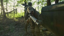 Two Soldiers In Military Uniform And Orange Glasses Moving In Green Forest During Tactical Action, Holding Weapons And Aiming Gun