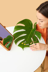 Poster - Young woman sitting at white table with stylish jewelry, palm leaf and mirror on color background