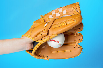 Baseball player holding ball with catcher's mitt on light blue background, closeup. Sports game